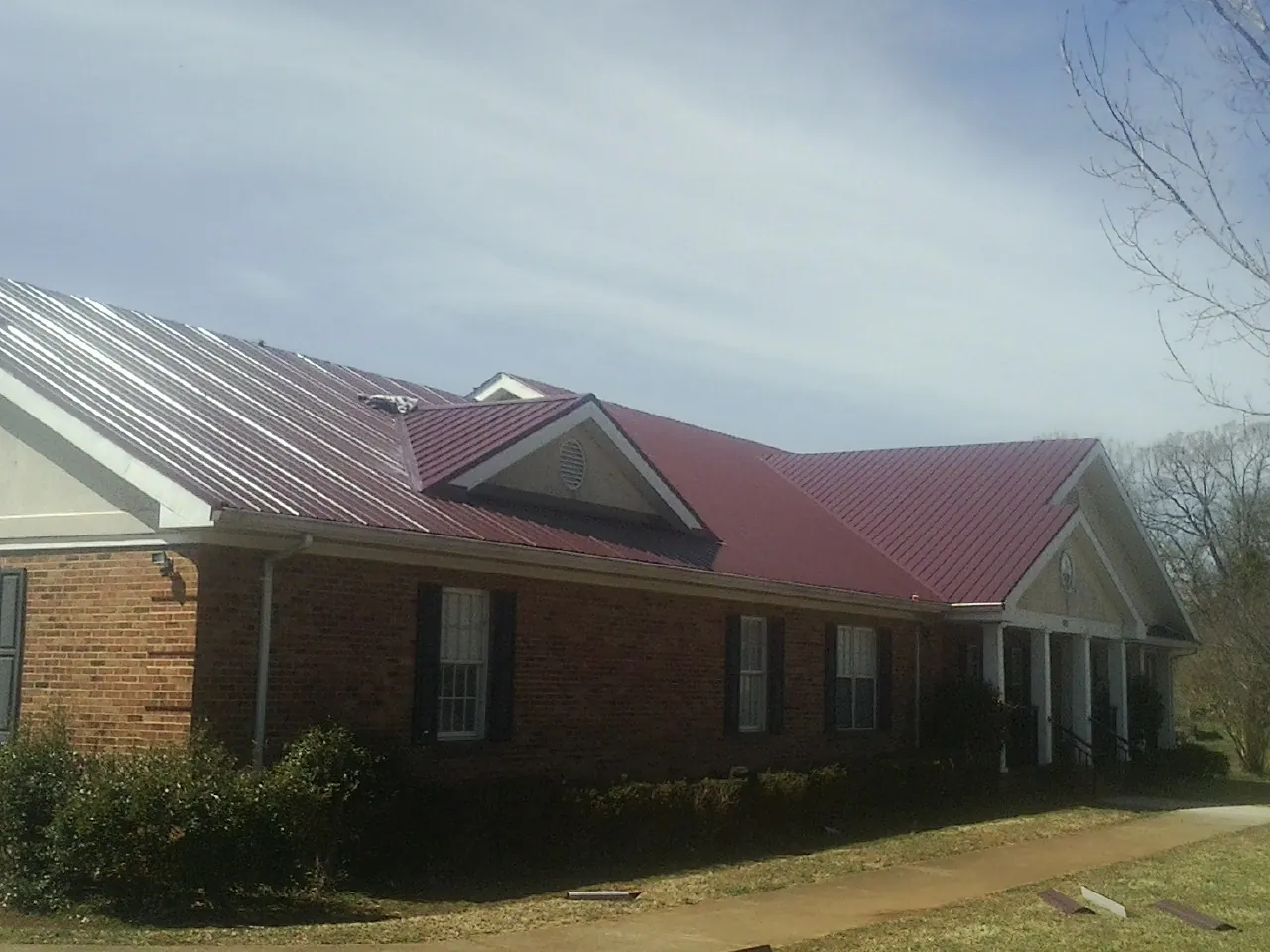 Red metal roof with gabled entries on a long brick building, from a Hail Damage Roof Repair job in Idaho City
