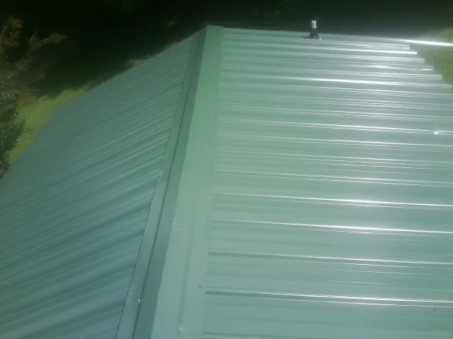 New green metal panels meeting at the ridge of a roof — Flat Roof Repair work by our crew in Idaho City