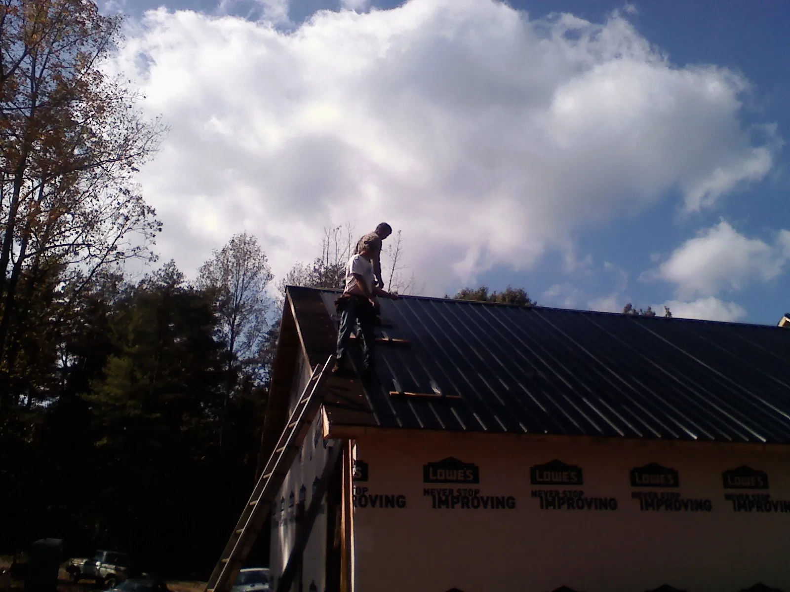 Roofer fastening dark metal panels high against a cloudy sky, from a Roof Inspection job in Idaho City