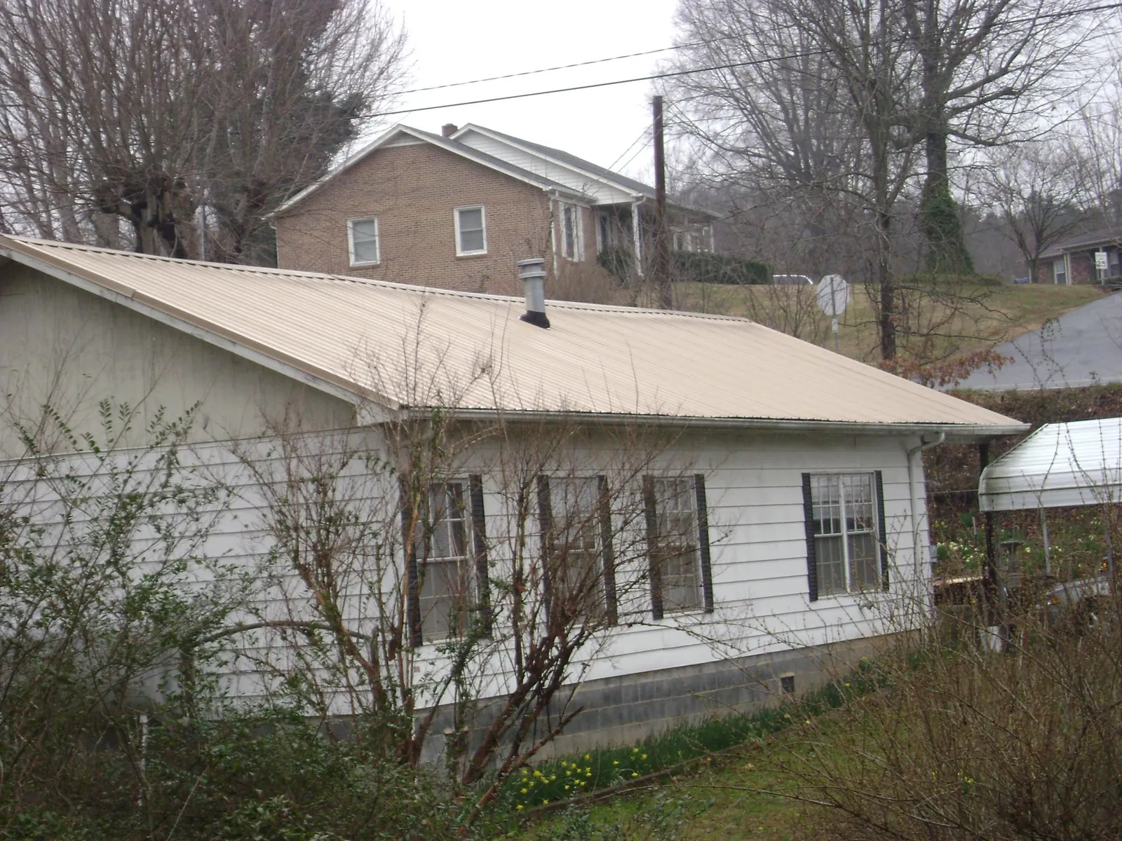 Tan metal roof on a white sided house set into a hillside — Commercial Roofing by Roofing Brothers in Idaho City